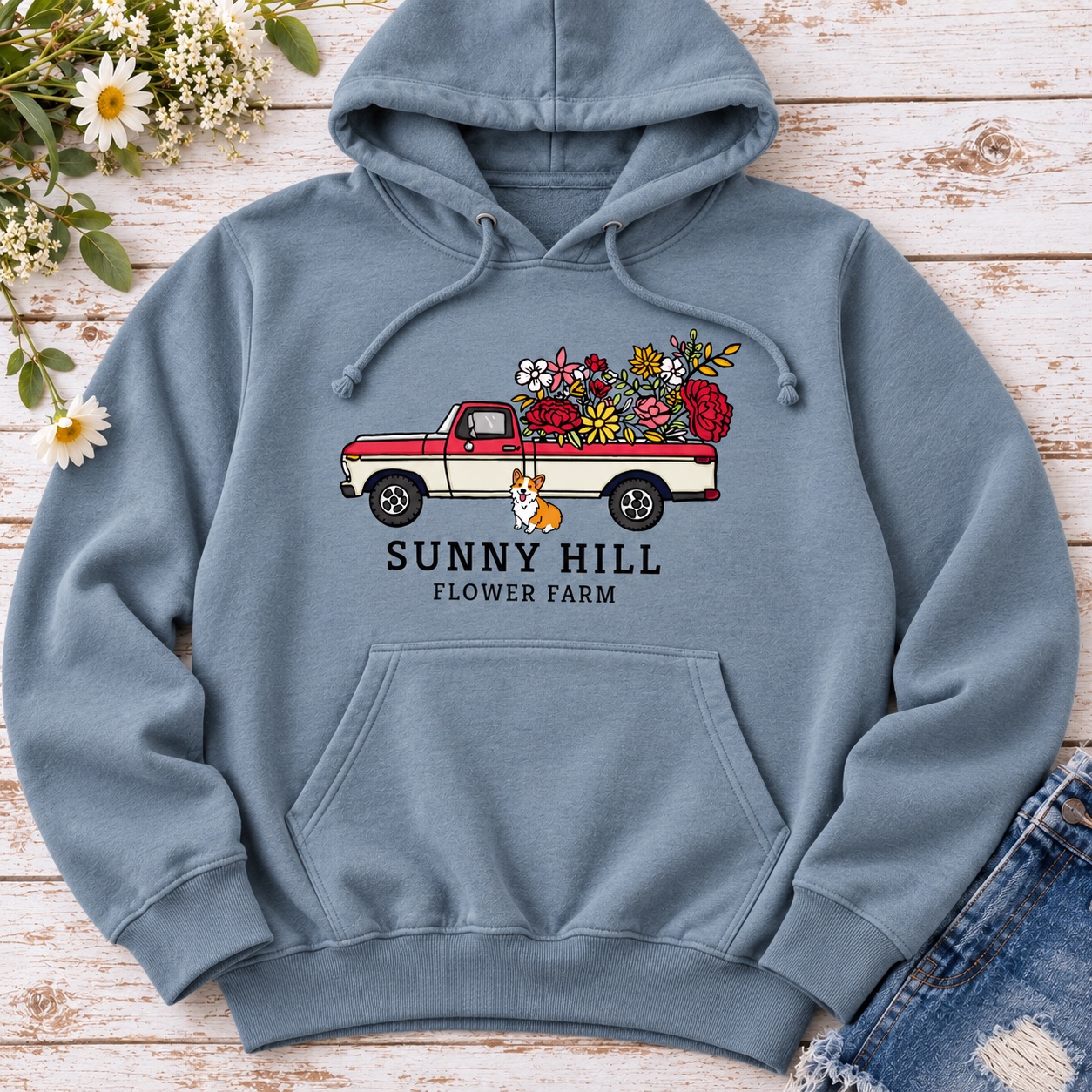 Styled flat-lay mockup of a blue-gray pullover hoodie with Micah’s Sunny Hill Flower Farm artwork